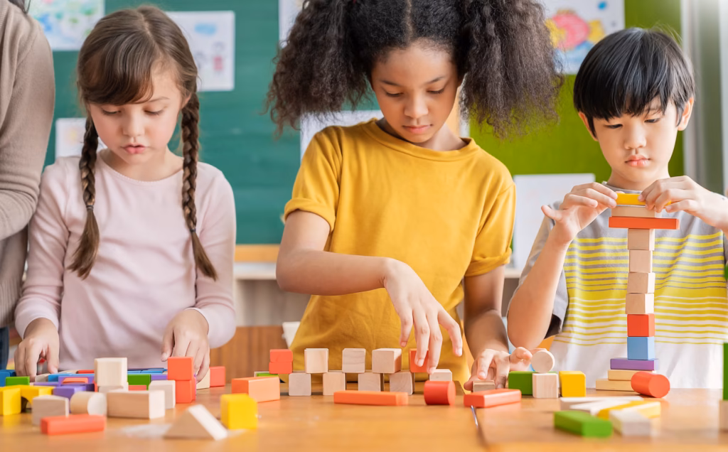 Three children building towers with wooden blocks at a table