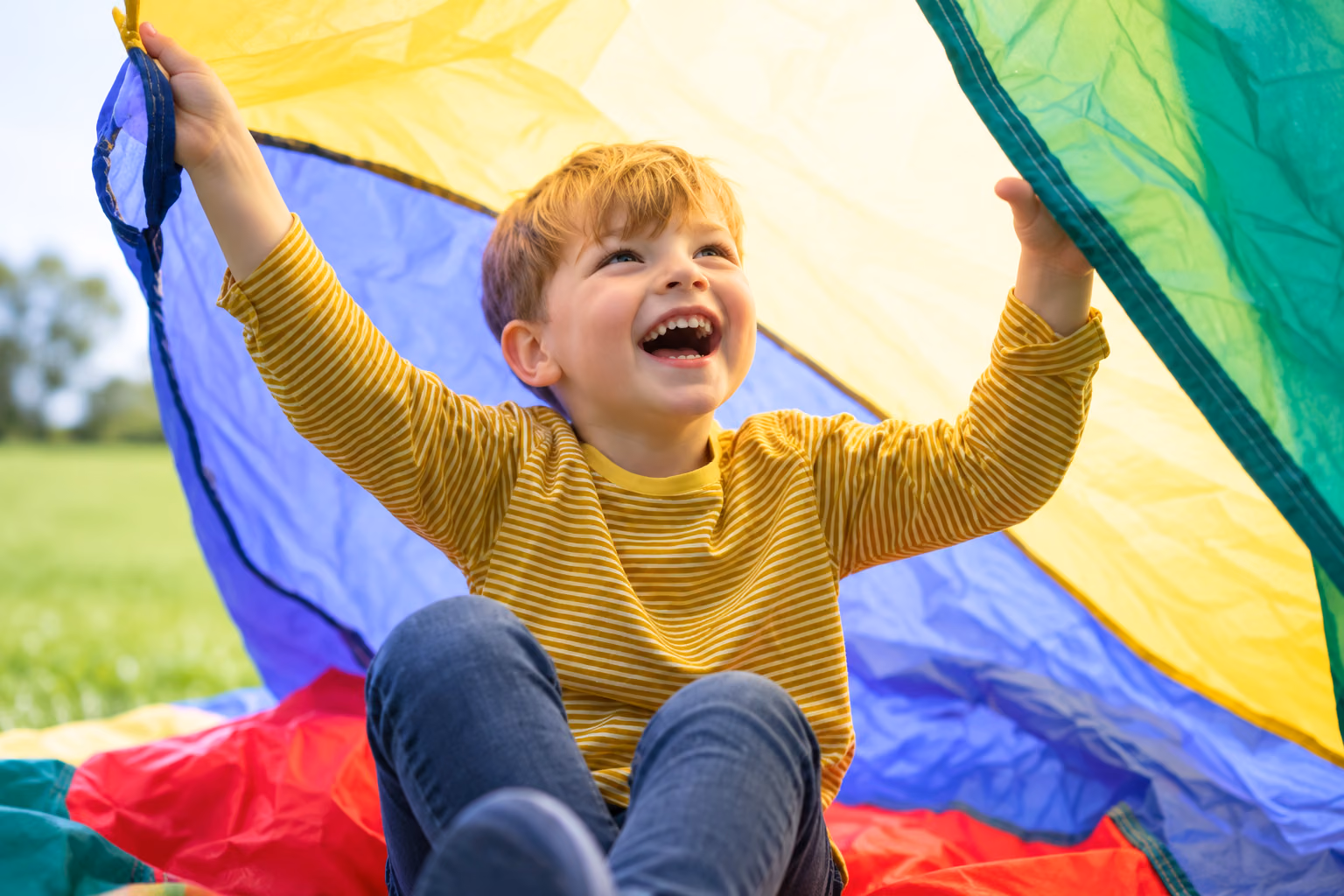 A laughing boy holding up a colorful play parachute outdoors