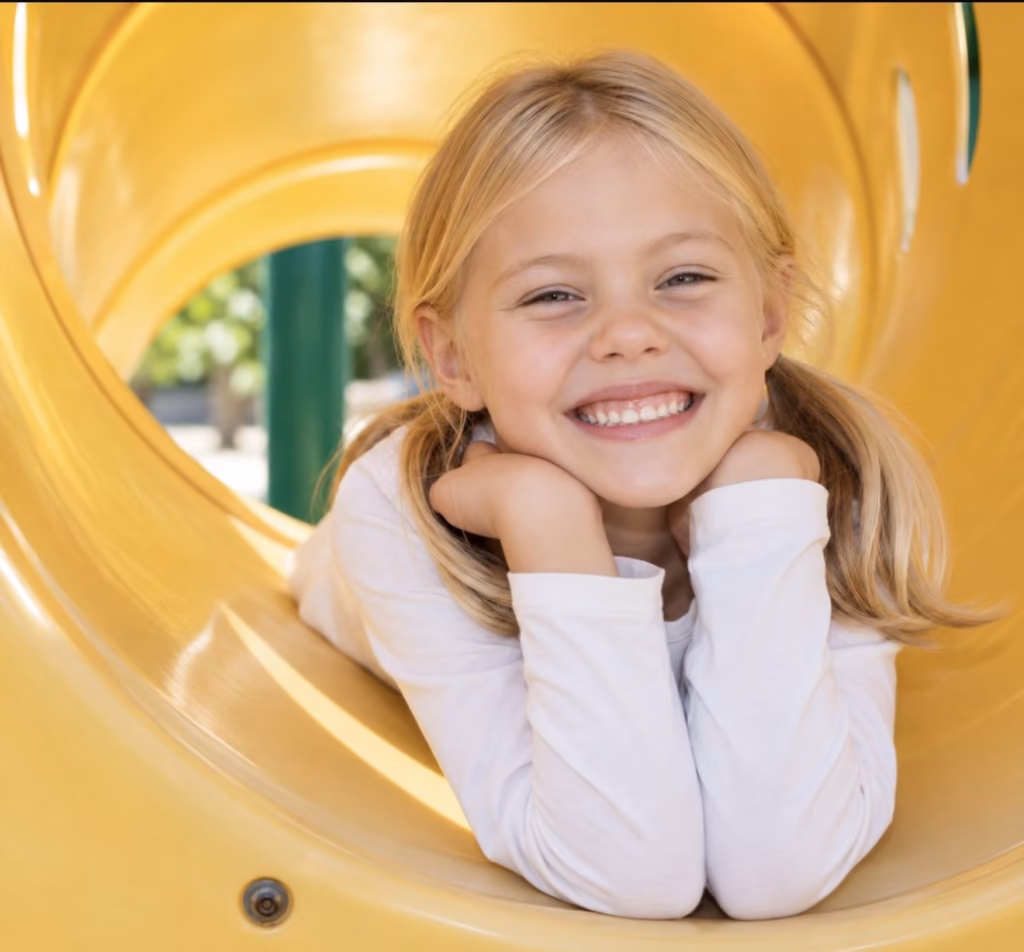 A smiling girl resting her chin on her hands inside a yellow play tunnel