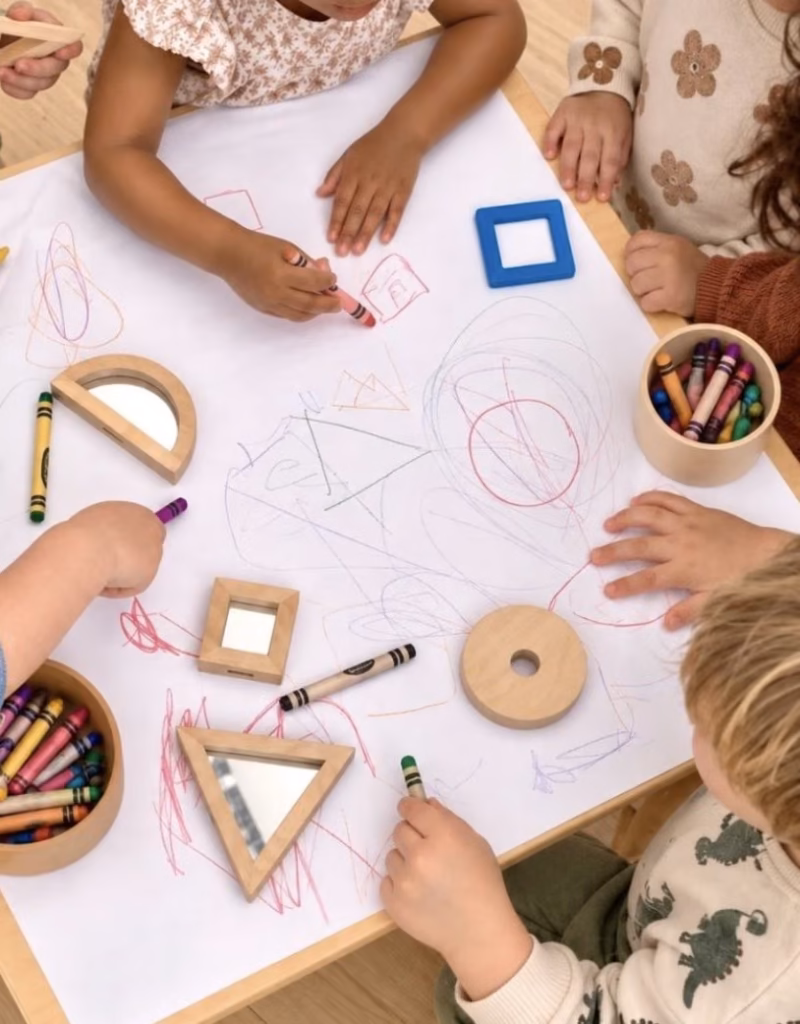 Children drawing together on a large sheet of paper around a table