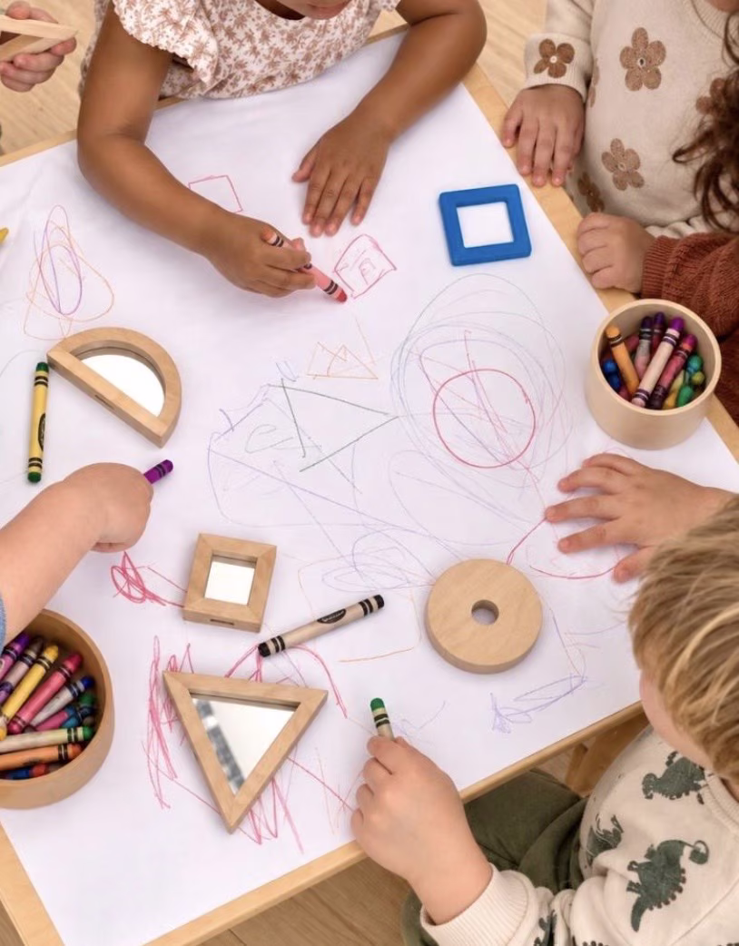 Children drawing together on a large sheet of paper around a table