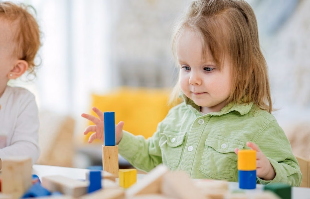 Toddler girl in a green shirt stacking wooden blocks
