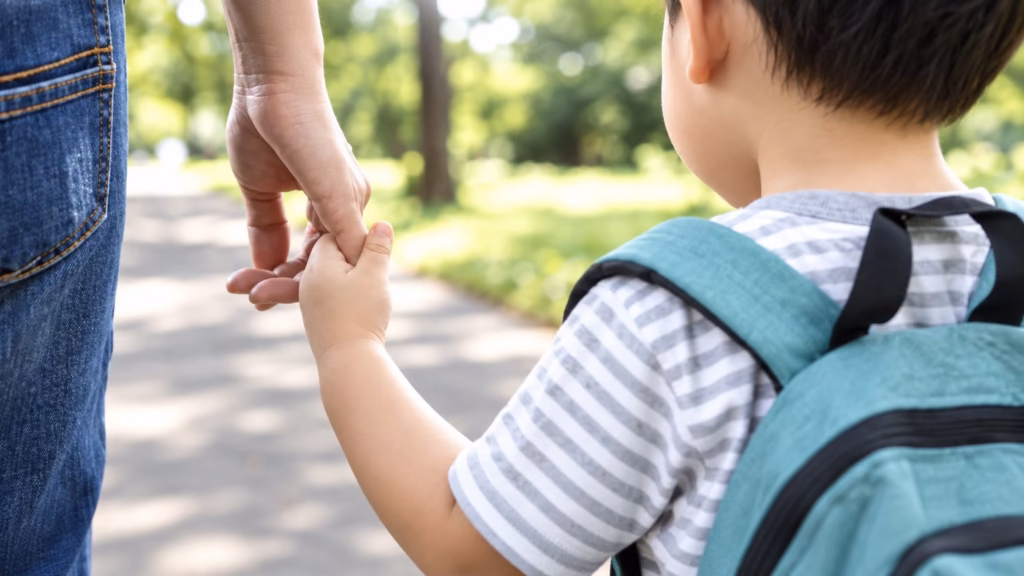 Child with a backpack holding a parent's hand on a sunny path