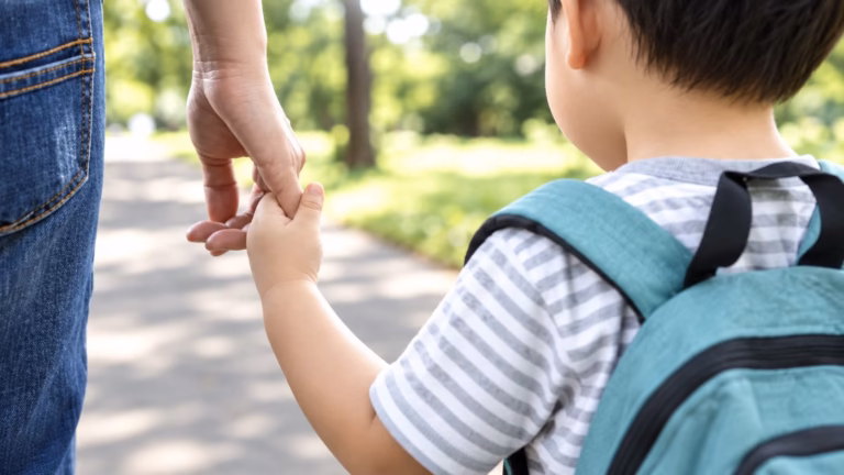 Child with a backpack holding a parent's hand on a sunny path