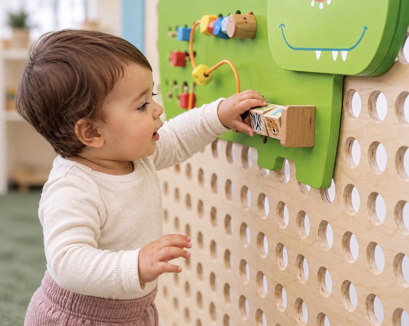 A toddler reaching for wooden blocks on a classroom activity wall