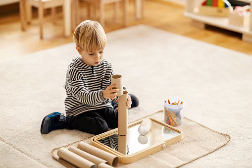 A little boy sitting on a rug building a tower with Montessori materials