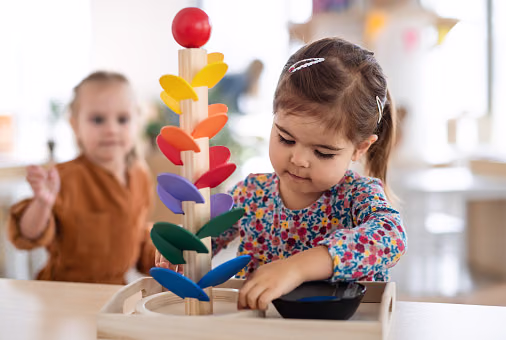 Two young children playing with a wooden marble run in a classroom